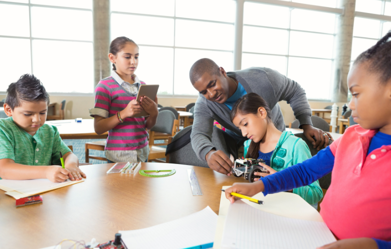 Group of children sitting at table with teacher working on projects