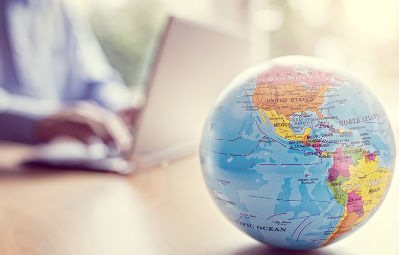 Close up on globe sitting on desk with a person on a laptop in the blurred background