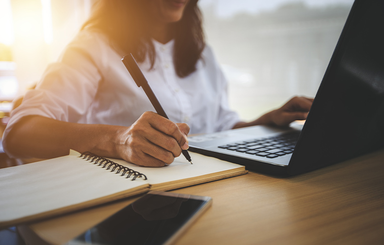 Woman researching on laptop and taking notes