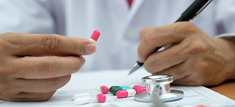 Close up of doctor writing on paper with pills and stethoscope in foreground