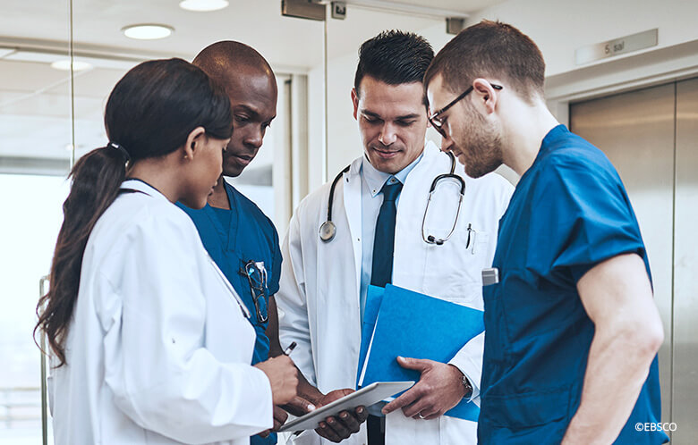 Group of medical professionals discussing while looking at a tablet in a hospital