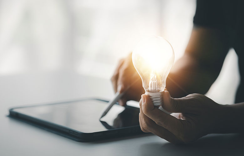 a person using a tablet and holding a lightbulb