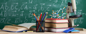 chalkboard with various math problems and books, pens, pencils, and microscope on a desk in front