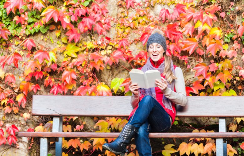 Woman reading a book on a bench with surrounded by fall foliage