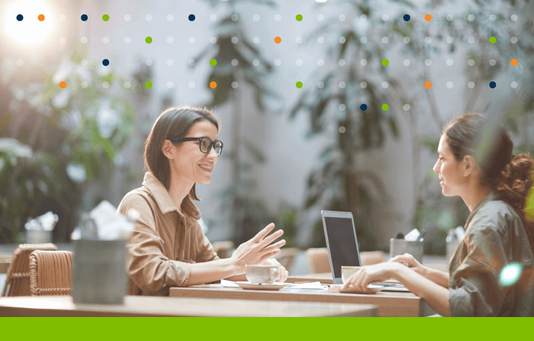 two women at coffee shop talking and working on laptop