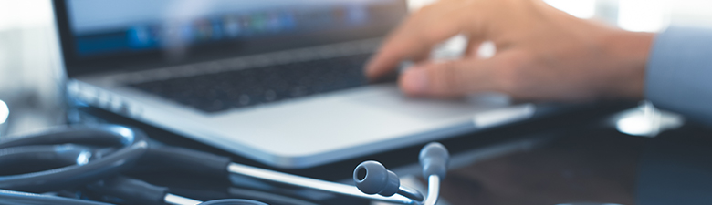 medical professional typing on a laptop with stethoscope on desk