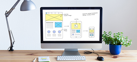 Desktop computer showing wireframe sketch of responsive web designs on multiple devices