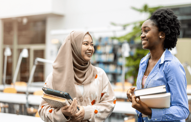 Two students holding textbooks in a campus library