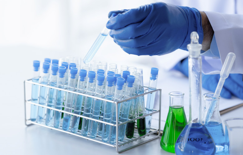 Close-up of a chemistry researcher's hands who are wearing gloves while using test tubes and beakers in lab