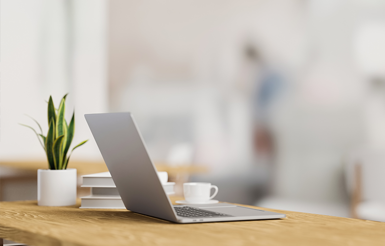 A laptop on a wood desk beside a cup and plant