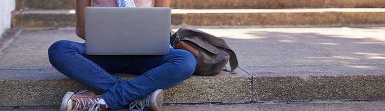 woman sitting on the steps of her college doing research on her laptop