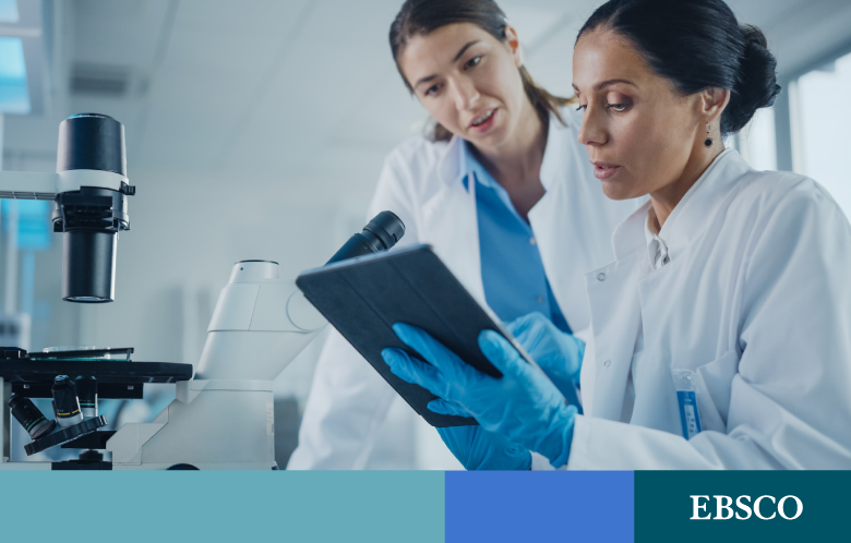 Two biomedical scientists researching on a tablet in front of a microscope