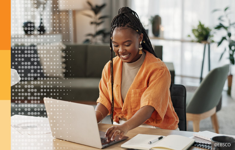 Woman sitting at a desk writing a blog on a laptop at home