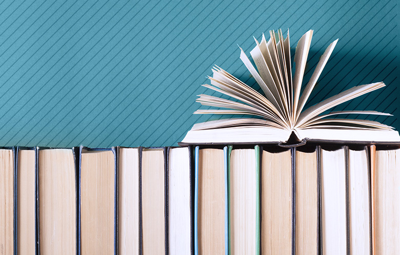 Hardcover books all lined up with an open book on top pages turning